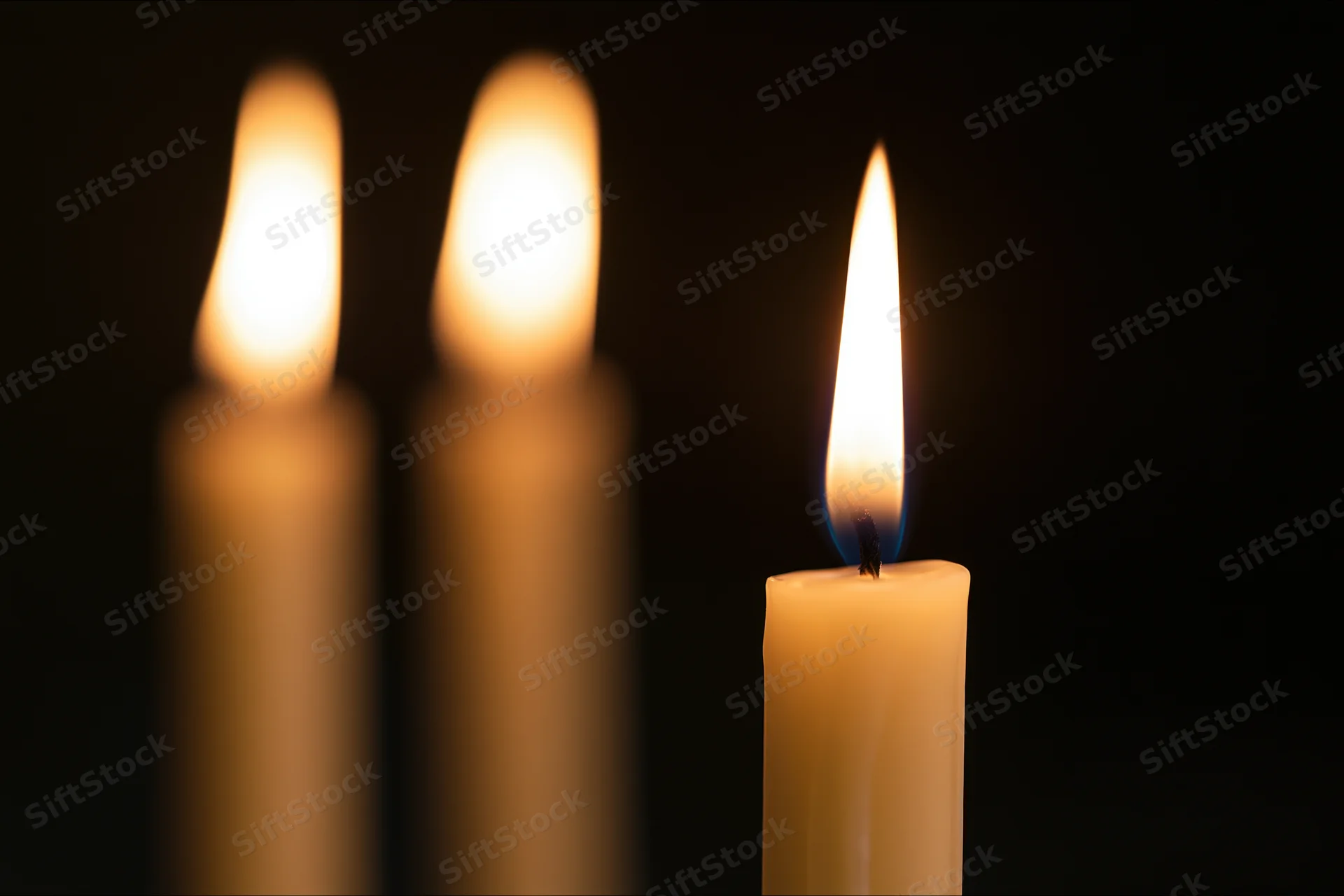 Three burning candles with one in focus against a dark background