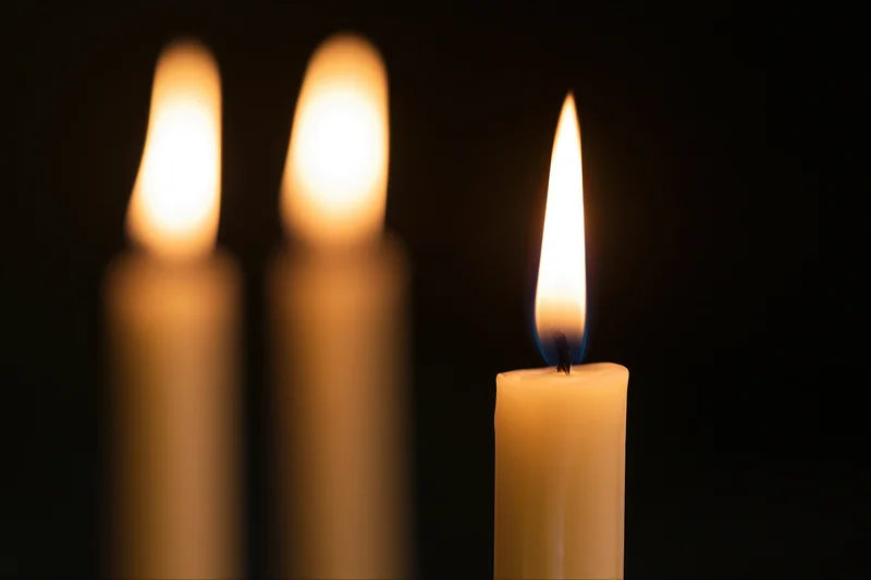 Three burning candles with one in focus against a dark background