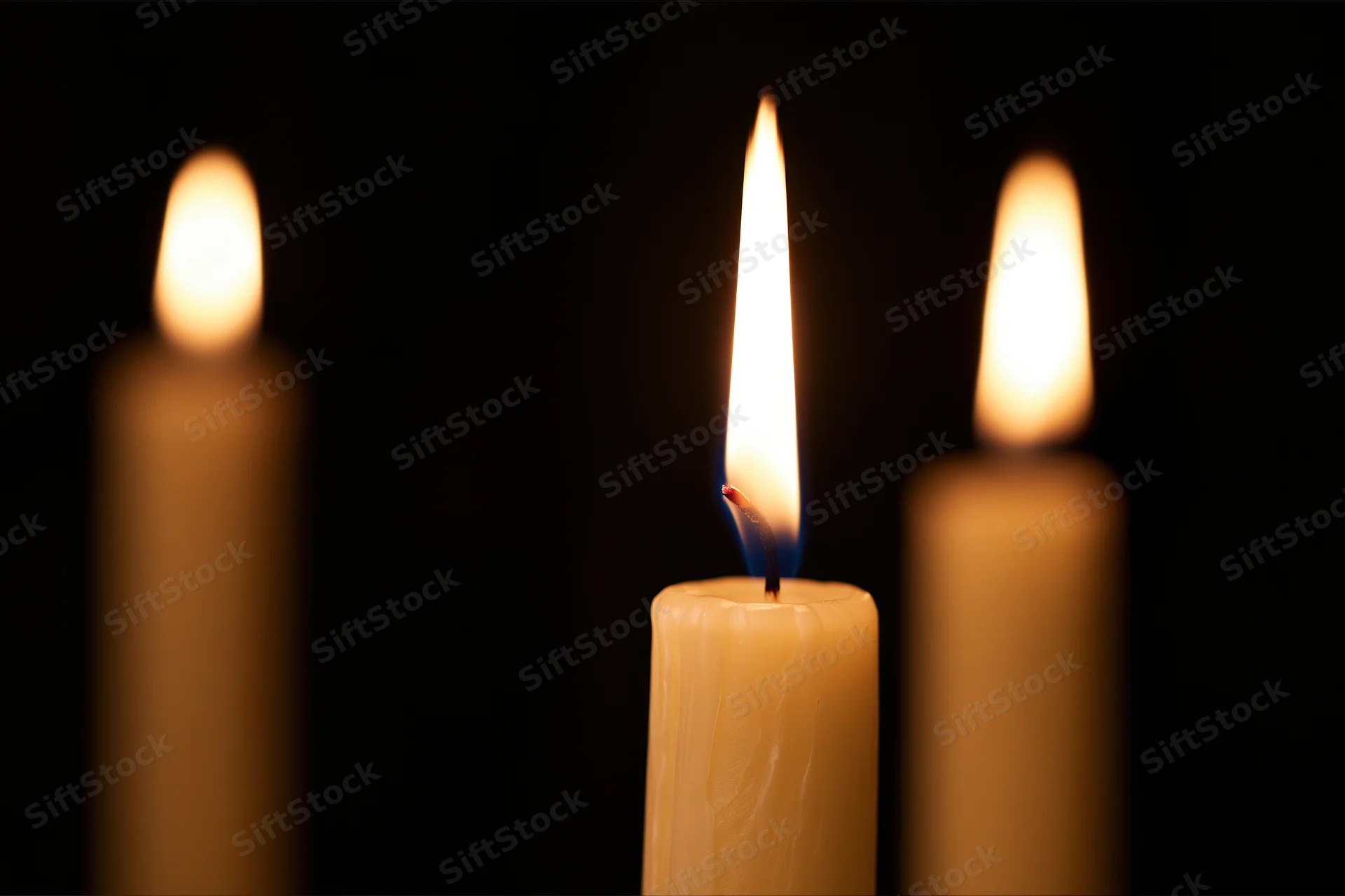 Three candles burning with one in focus against a dark background