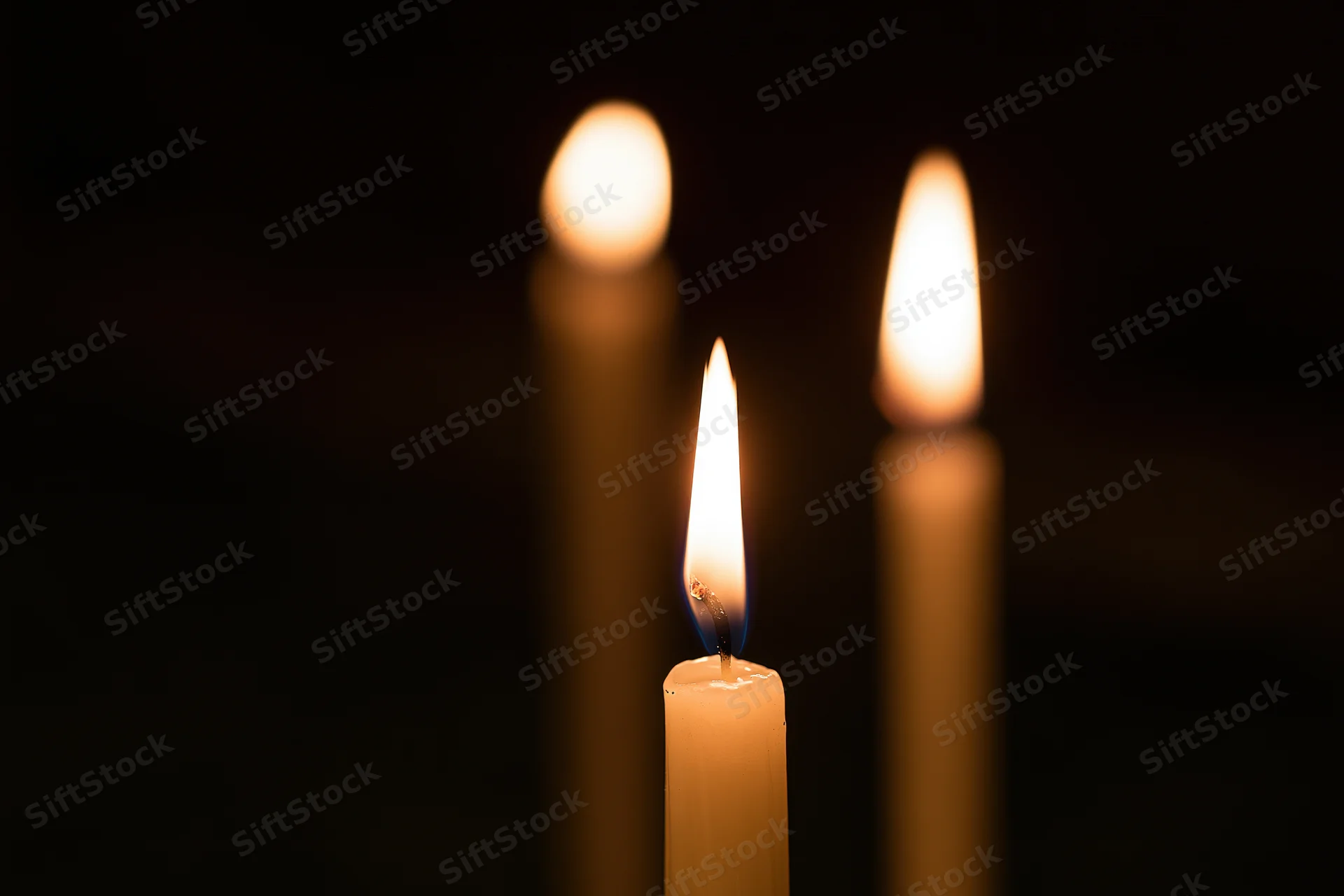 Three thin wax candles burning with one in focus against a dark background
