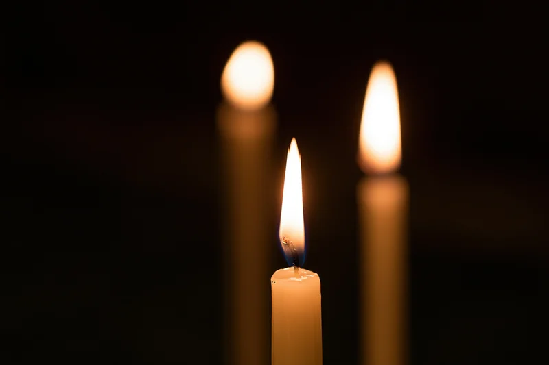 Three thin wax candles burning with one in focus against a dark background