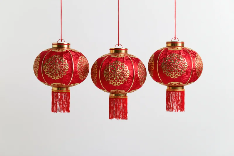Three red and gold chinese paper lanterns hanging in a row against a white background
