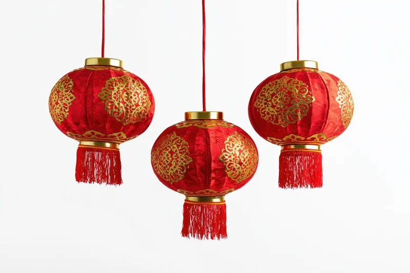 Three red and gold chinese paper lanterns hanging in a row against white background