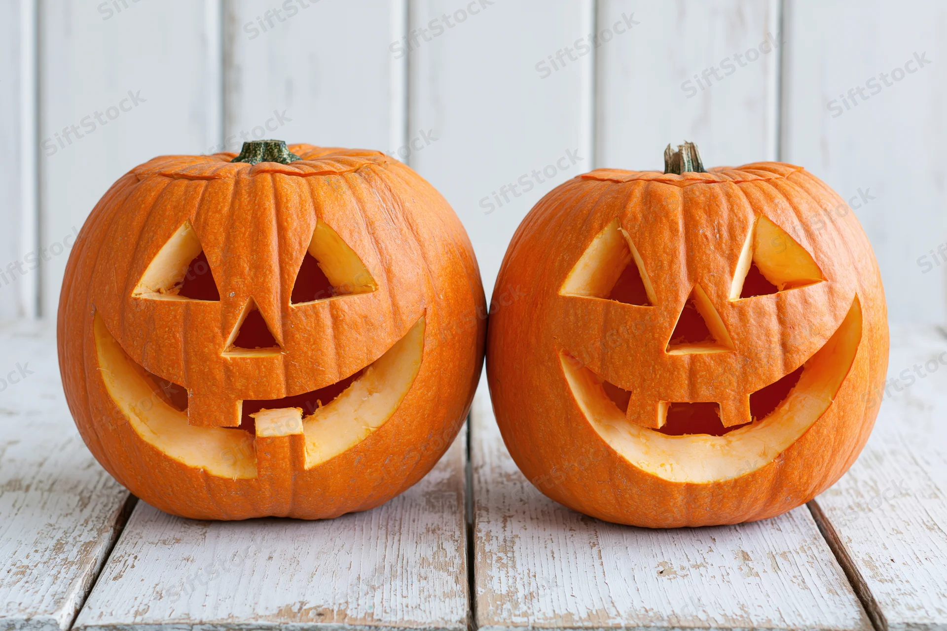 Two carved pumpkins with smiling faces on a white wooden table