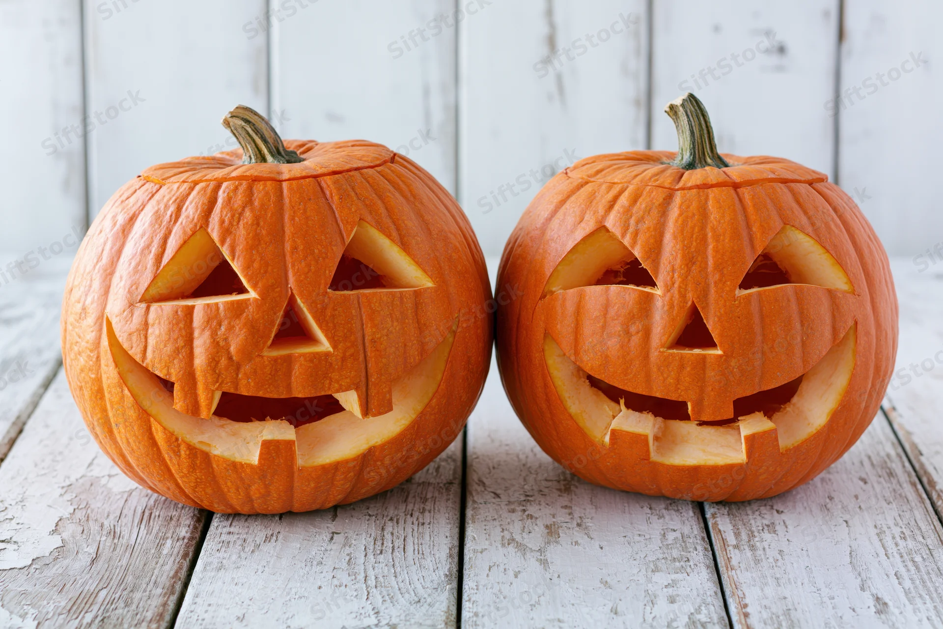 Two carved pumpkins with smiling faces on a white wooden table