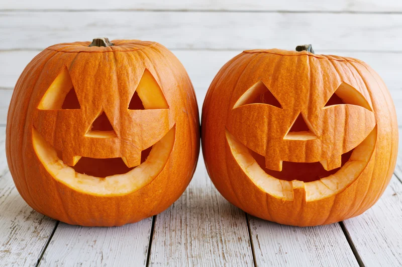 Two carved pumpkins with smiling faces on a white wooden surface