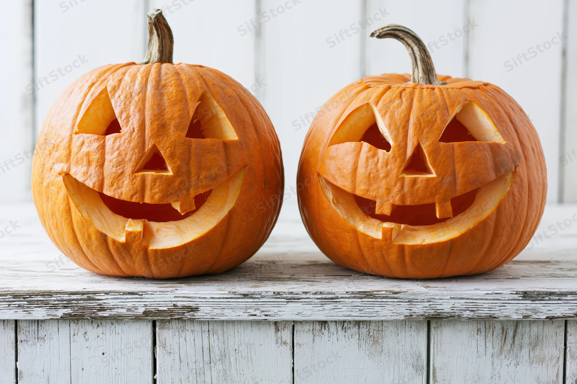 Two carved pumpkins with smiling faces on a white wooden table