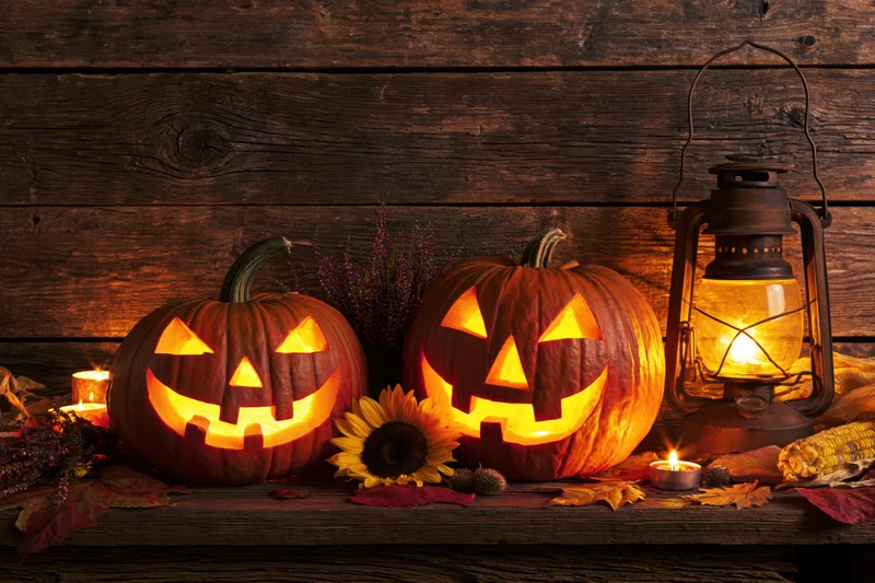 Two carved jack-o-lanterns glowing on a wooden table with candles, lantern, and autumn decorations