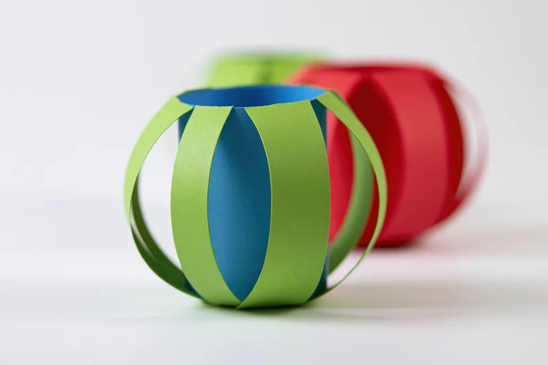Handmade paper lanterns with green and blue stripes on a white surface