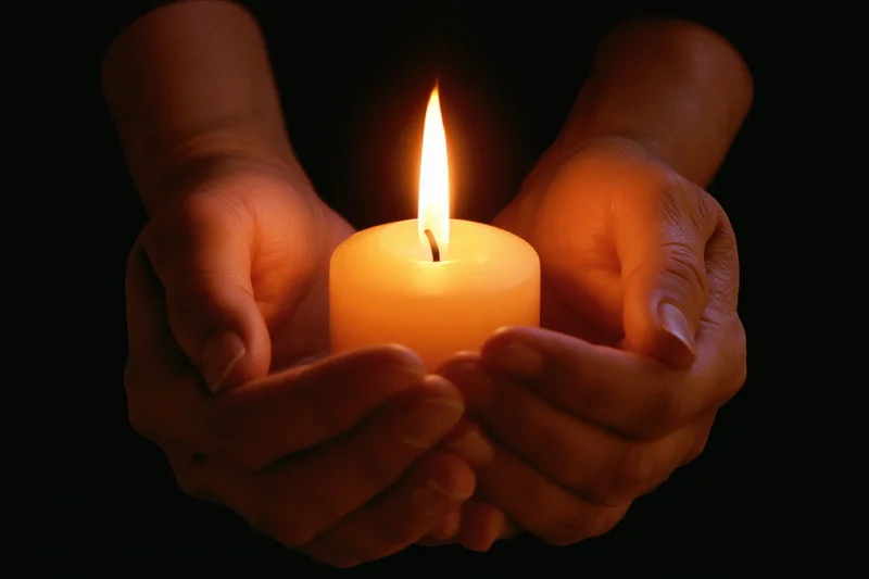 Hands cupping a lit candle in darkness