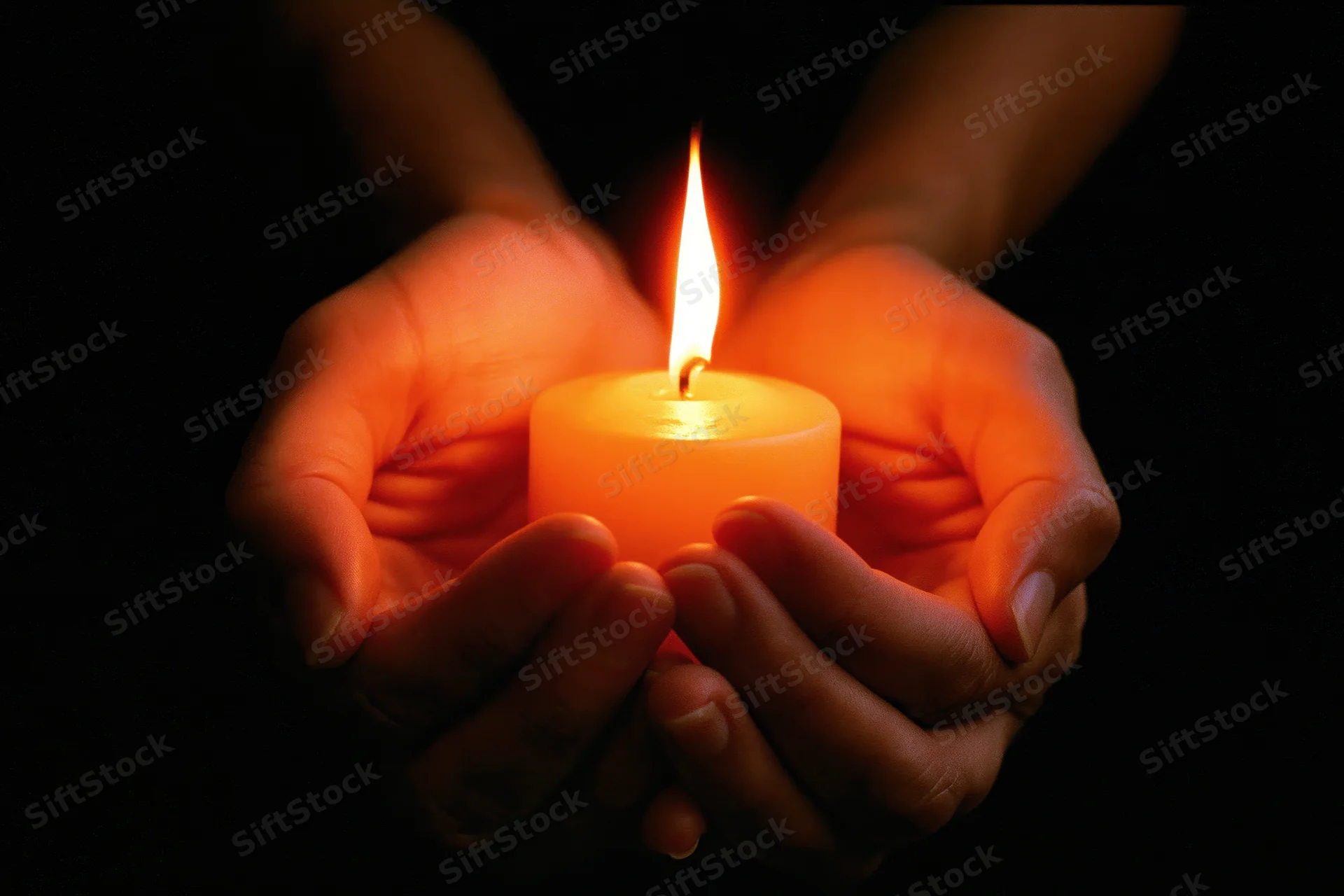 Hands cupping a lit candle in the dark