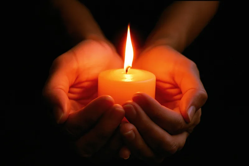 Hands cupping a lit candle in the dark