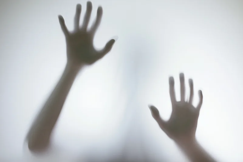 Hands pressing against frosted glass in a dimly lit interior