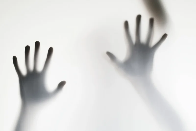 Two hands pressing against frosted glass with blurred shadows and soft light