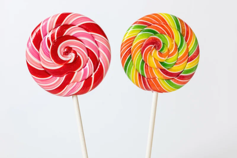 Two large round swirl lollipops on white sticks placed side by side against white background