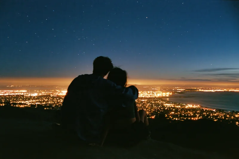 Couple embracing on hilltop overlooking city lights at night