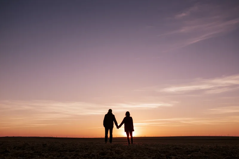 Couple holding hands silhouetted against sunset sky in open field