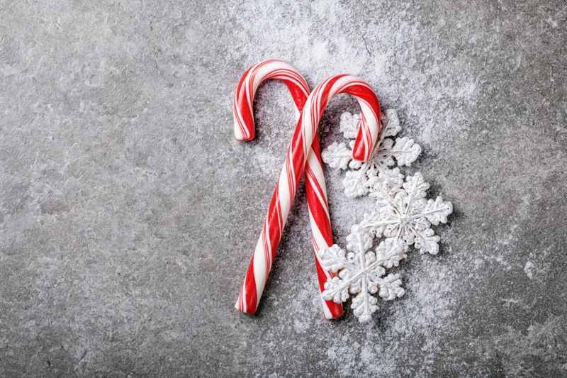 Two red and white striped candy canes crossed with white snowflakes on a gray textured surface