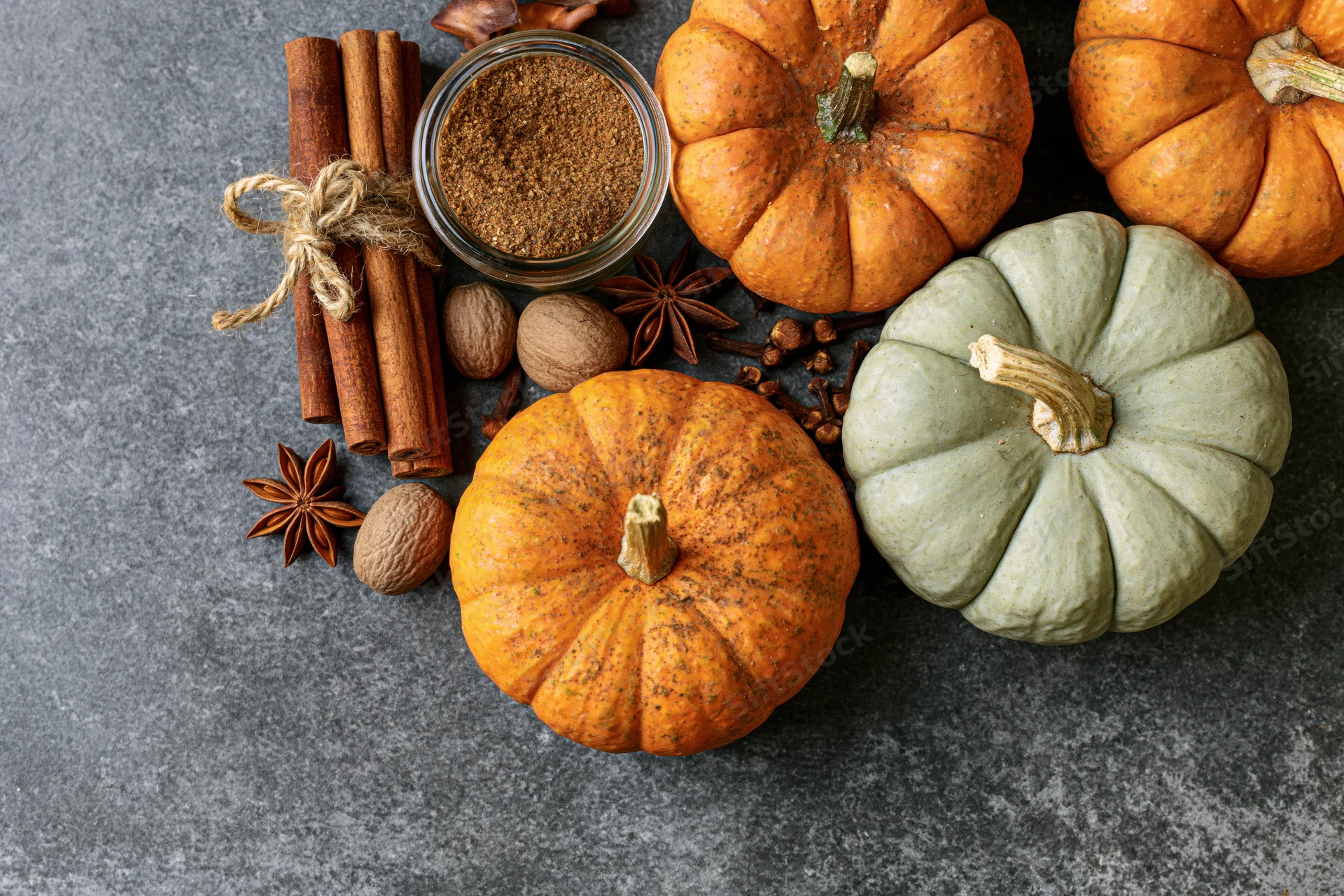 Small pumpkins and spices arranged on a dark countertop for autumn cooking