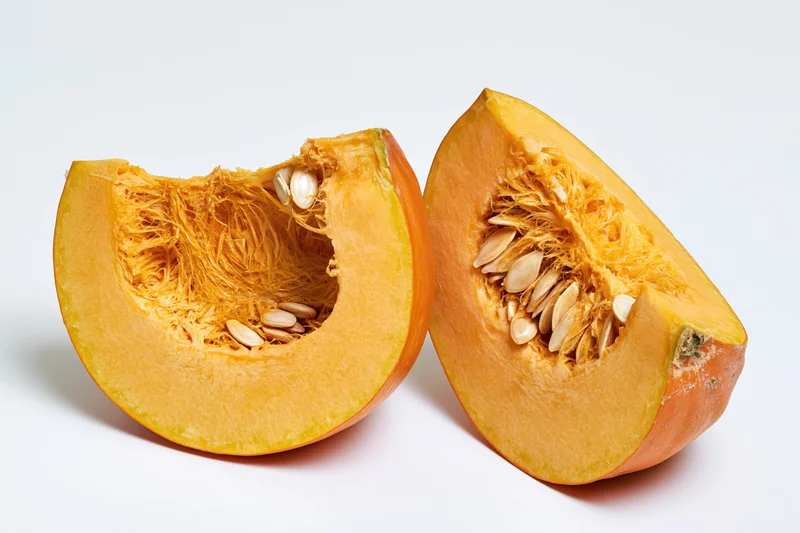 Two wedge-shaped pumpkin slices cut to reveal fibrous interior and seeds on white background