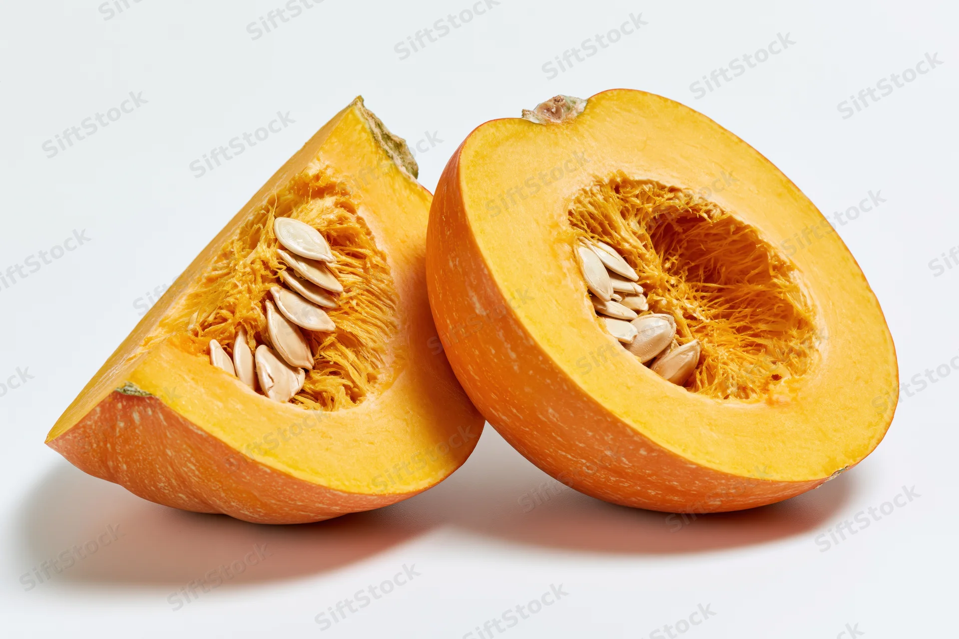 Two pumpkin slices cut to reveal fibrous interior and seeds on white background
