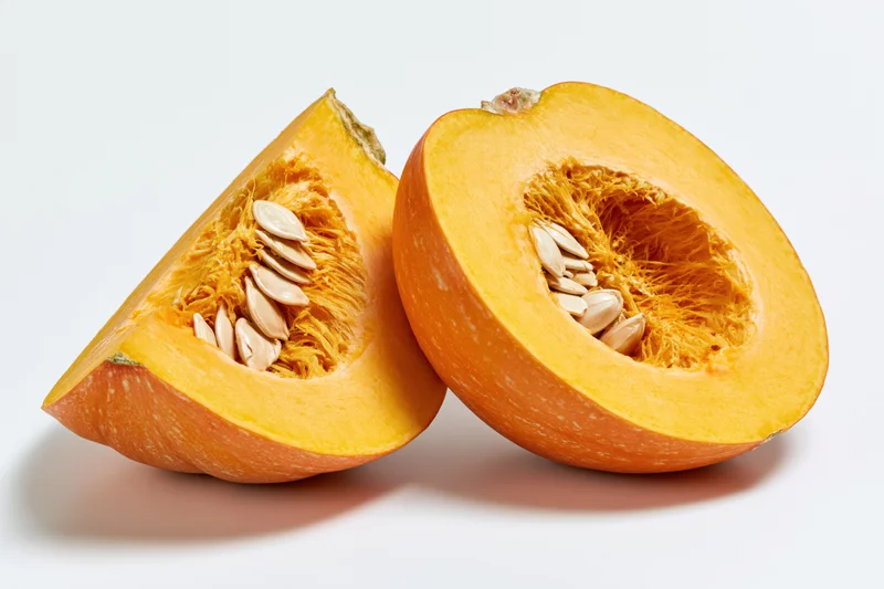 Two pumpkin slices cut to reveal fibrous interior and seeds on white background