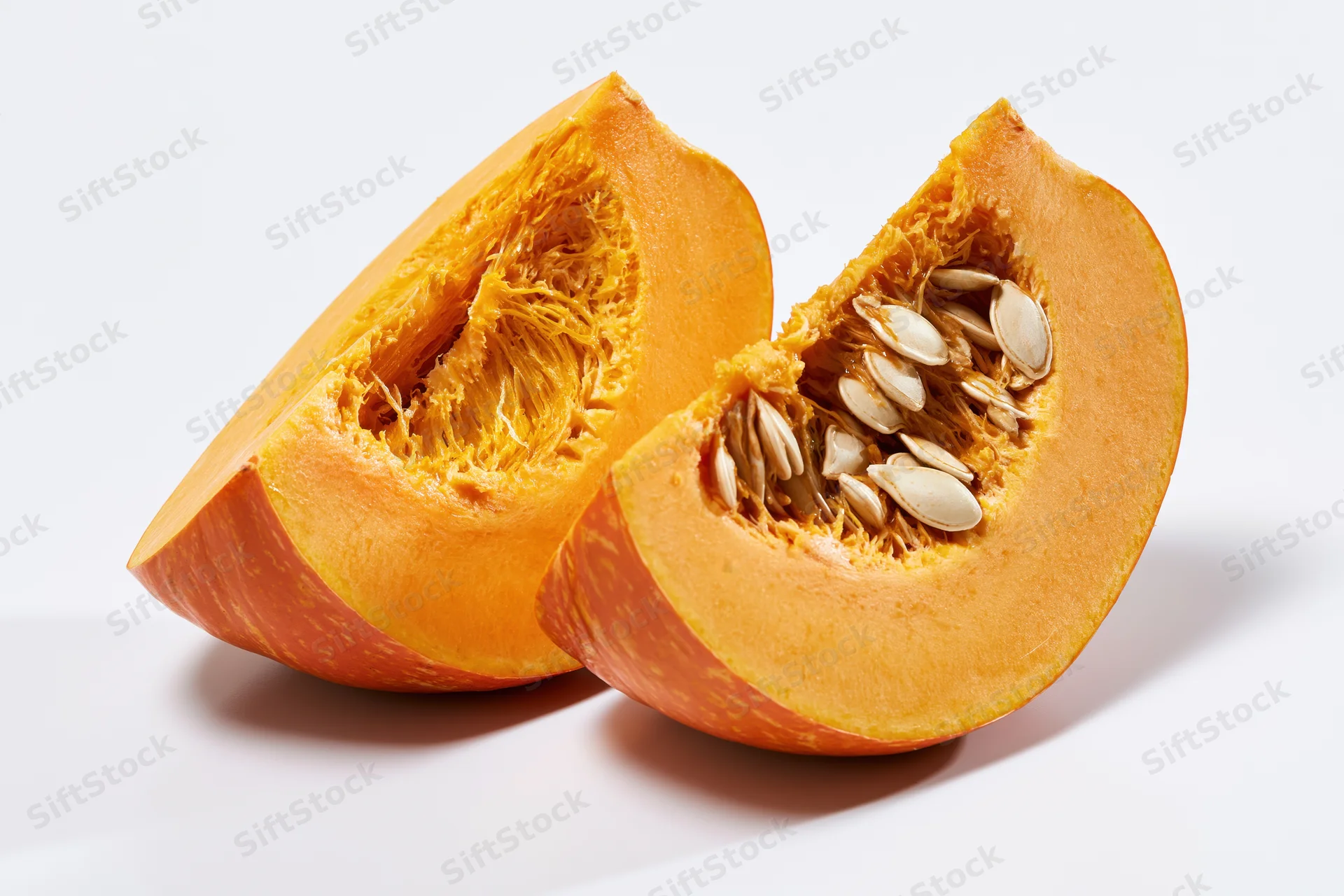 Two wedge-shaped pumpkin slices cut to reveal fibrous interior and seeds on white background