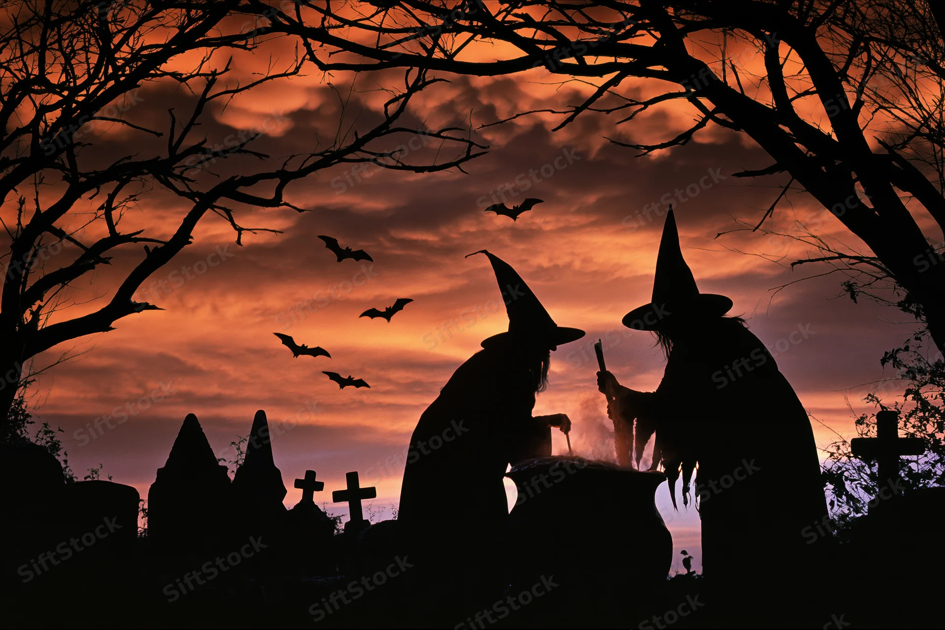 Two witches in pointed hats stirring a cauldron in a graveyard at twilight