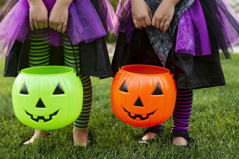 Two young girls in witch costumes holding plastic pumpkin buckets on grass during halloween