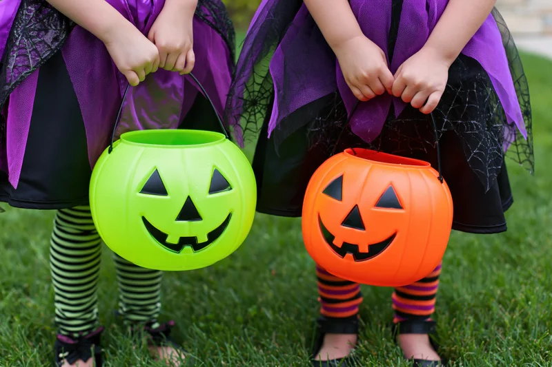 Two young girls in witch costumes holding plastic pumpkin buckets on grass