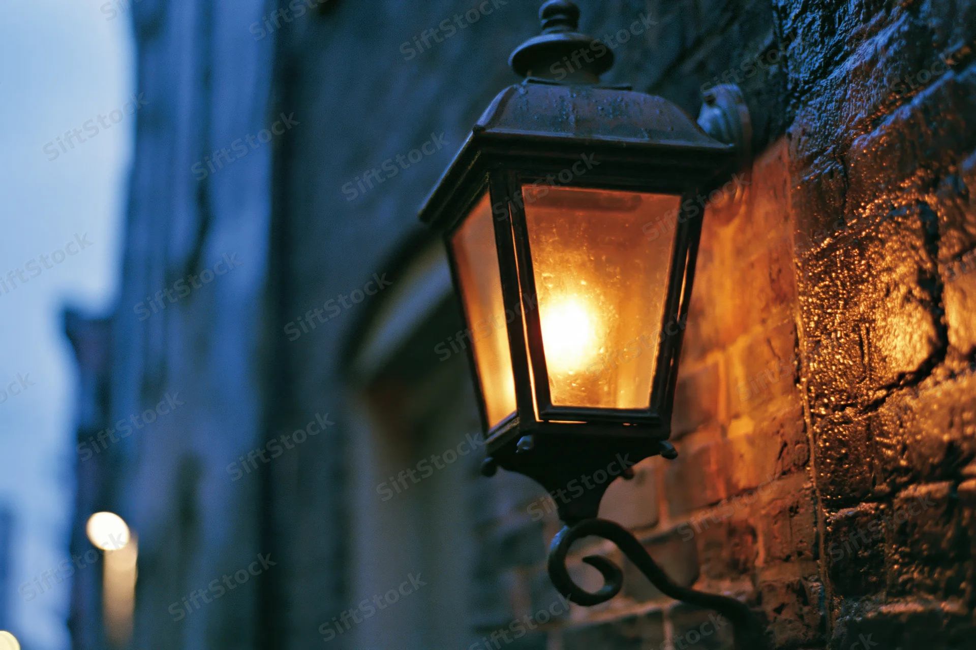 Vintage castiron lantern glowing on a wet brick building exterior at dusk