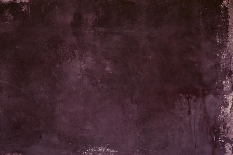Weathered concrete wall surface with dark purple and gray stains and cracks filling the frame