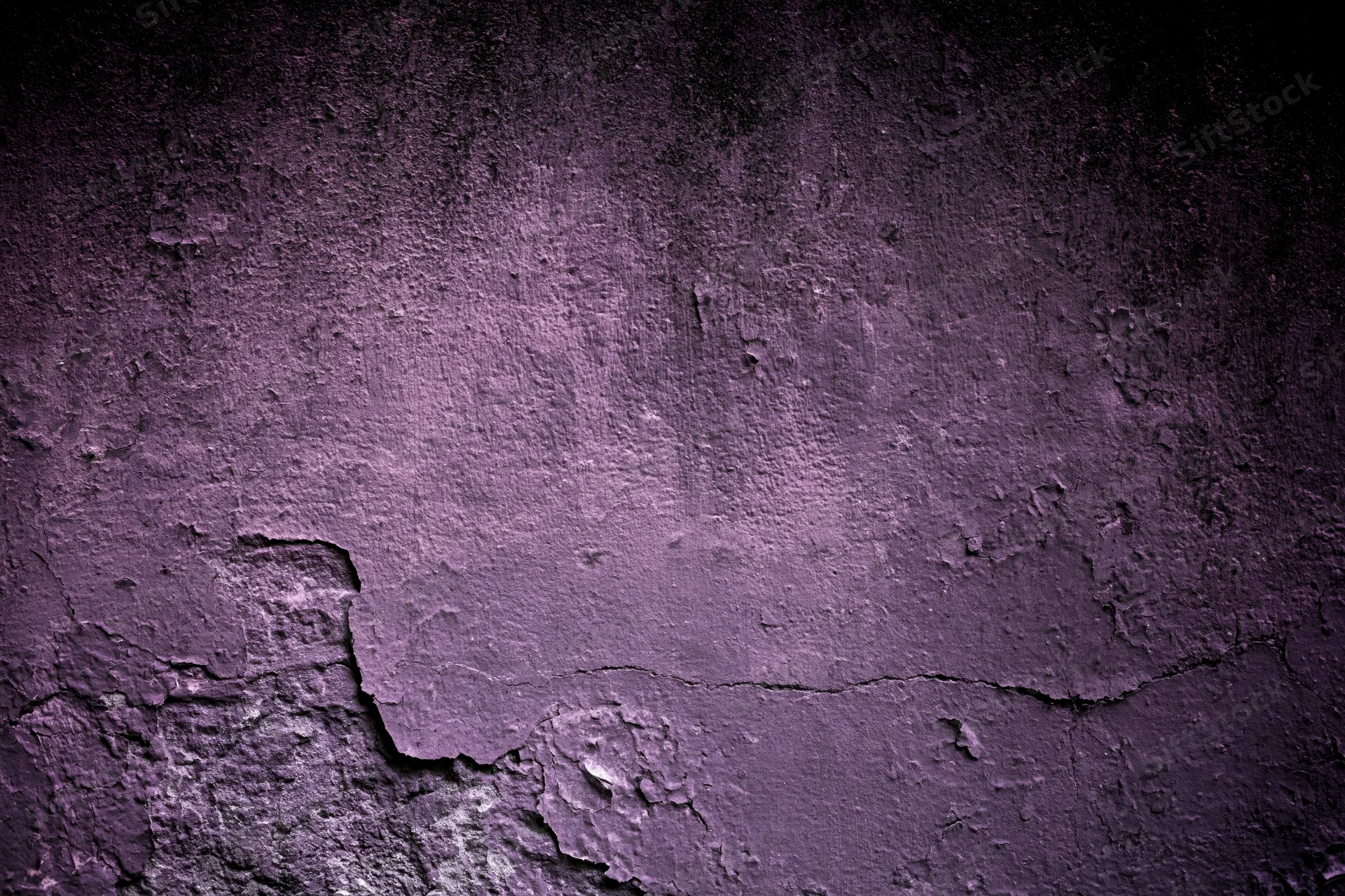 Weathered concrete wall with peeling purple paint and cracks, showing textured surface and decay