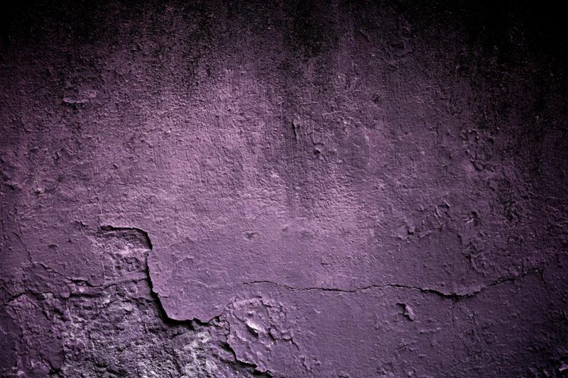 Weathered concrete wall with peeling purple paint and cracks, showing textured surface and decay