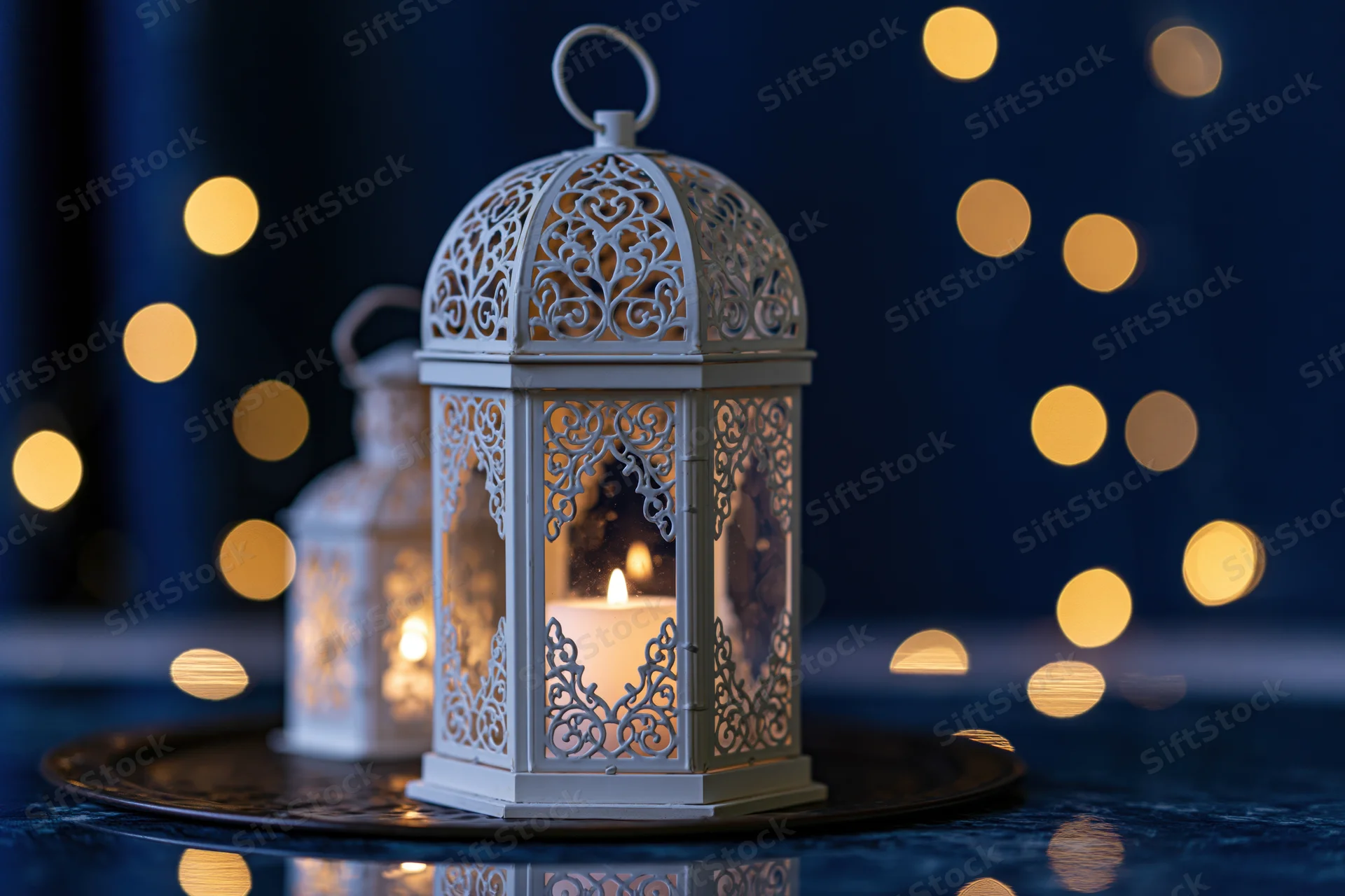 White ornate moroccan lantern with lit candle on dark reflective surface against bokeh lights