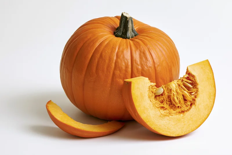 Whole orange pumpkin with a cut wedge slice leaning against it on white background