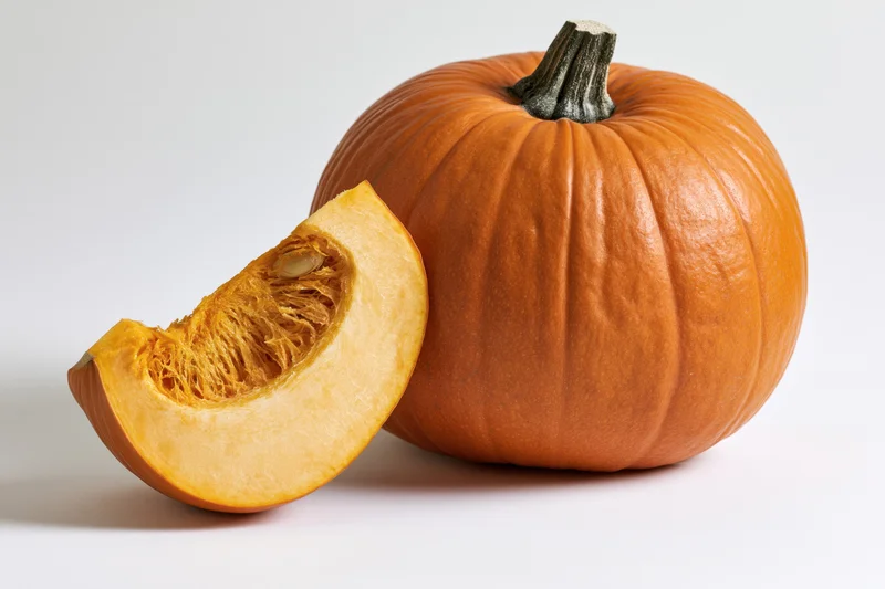 Whole orange pumpkin with a cut wedge slice leaning against it on a white background