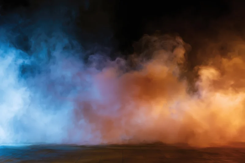 Colored smoke billowing and drifting above a wooden floor in a dark studio space