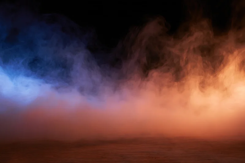 Colored smoke drifting above a dark surface with blue and orange hues