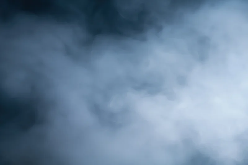 Wisps of white smoke drifting and swirling in a dark atmosphere