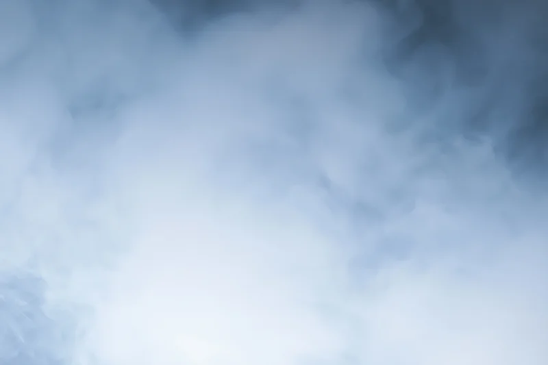 Wisps of white smoke drifting and swirling in a soft hazy atmosphere