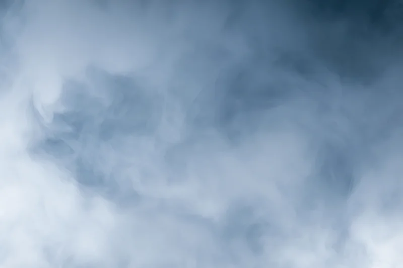 Wisps of white smoke drifting and swirling in a hazy blue atmosphere