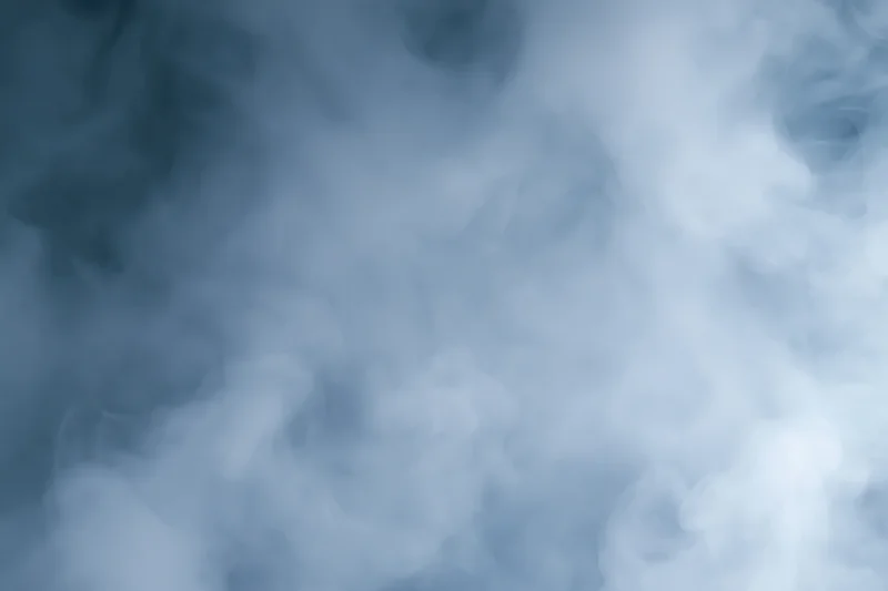 Wisps of white smoke drifting and swirling in a hazy blue atmosphere
