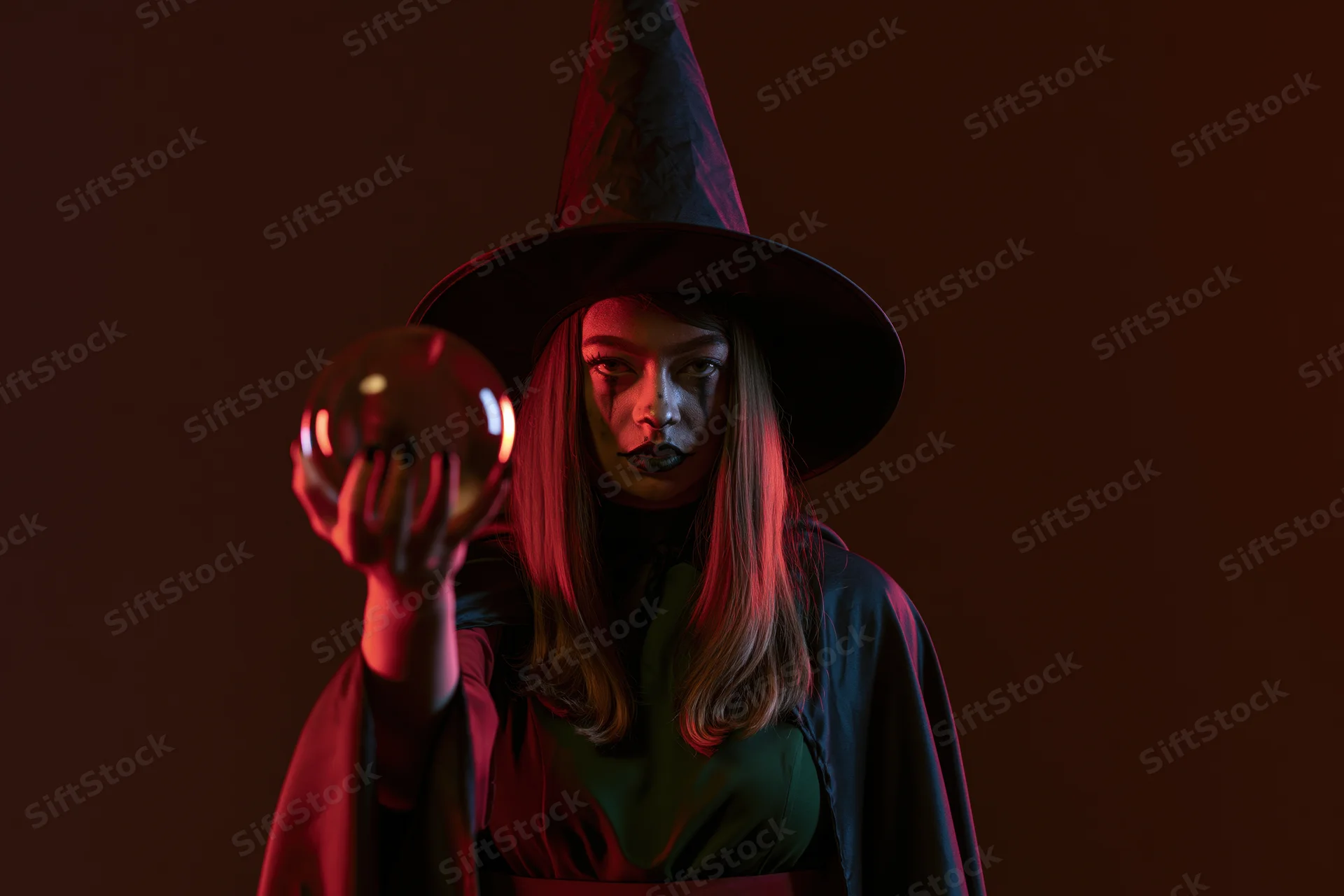 Woman in witch costume holding crystal ball under red lighting