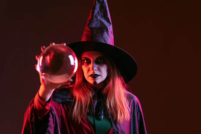 Woman in witch costume holding crystal ball against dark background