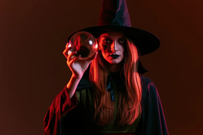 Woman in witch costume holding crystal ball under red lighting in studio
