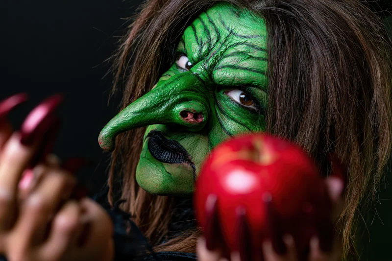 Woman in green witch makeup holding red apple with clawed hand