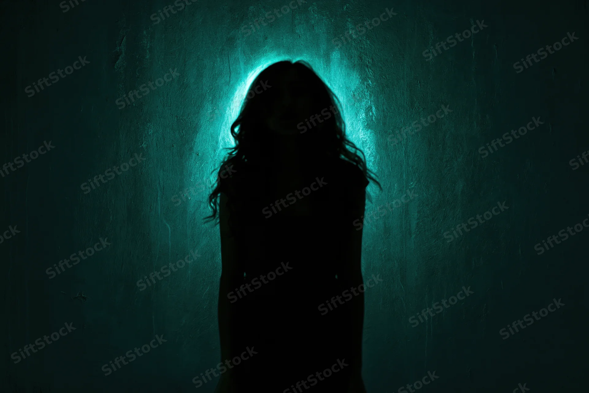 Silhouette of a woman standing still against a textured wall illuminated by a teal backlight