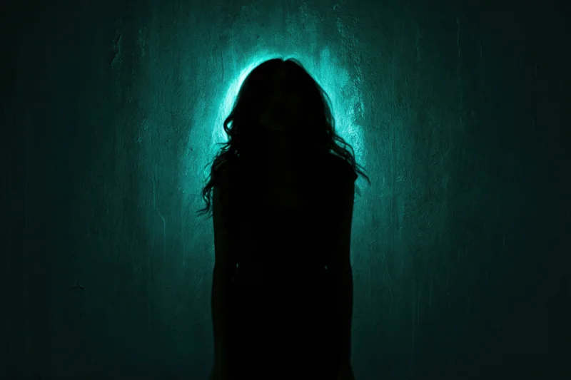 Silhouette of a woman standing still against a textured wall illuminated by a teal backlight