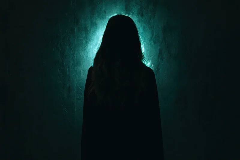 Woman in silhouette standing backlit by teal light against dark textured wall